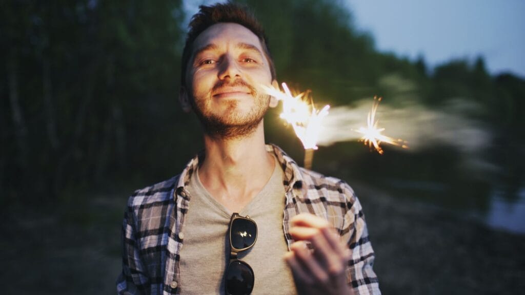 Man with sparkler enjoying an evening outdoors with a joyful expression.