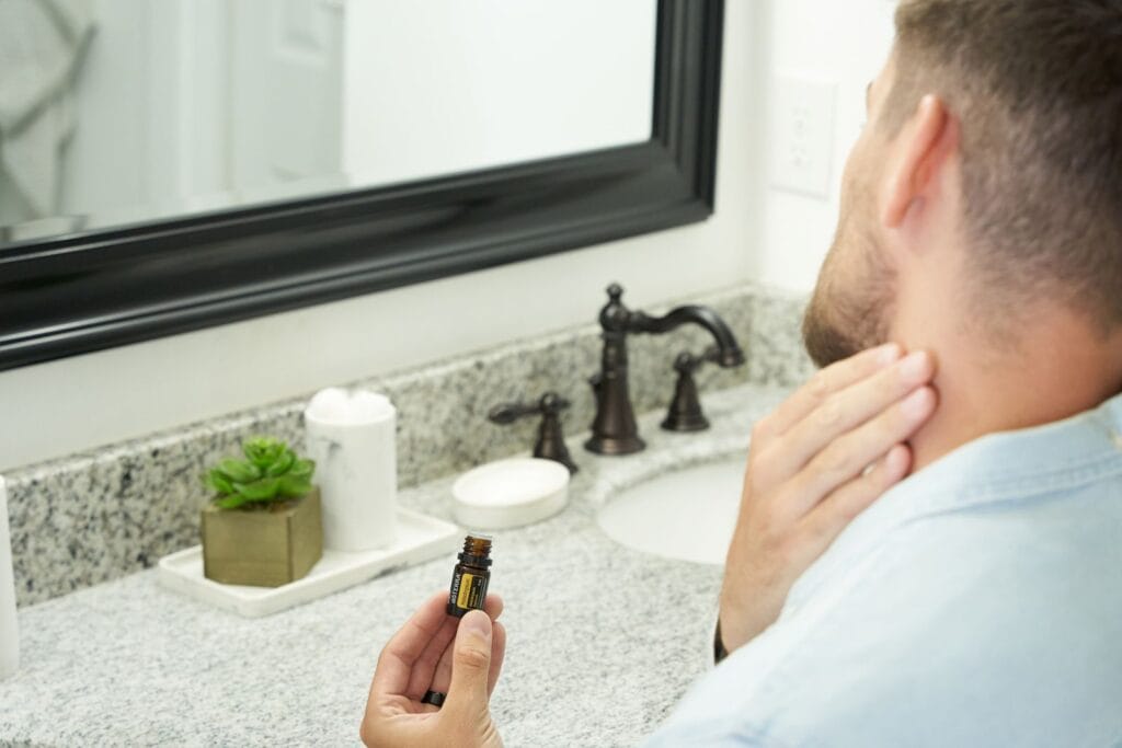 Adult man in bathroom holding an essential oil bottle near mirror, focusing on grooming and self-care.