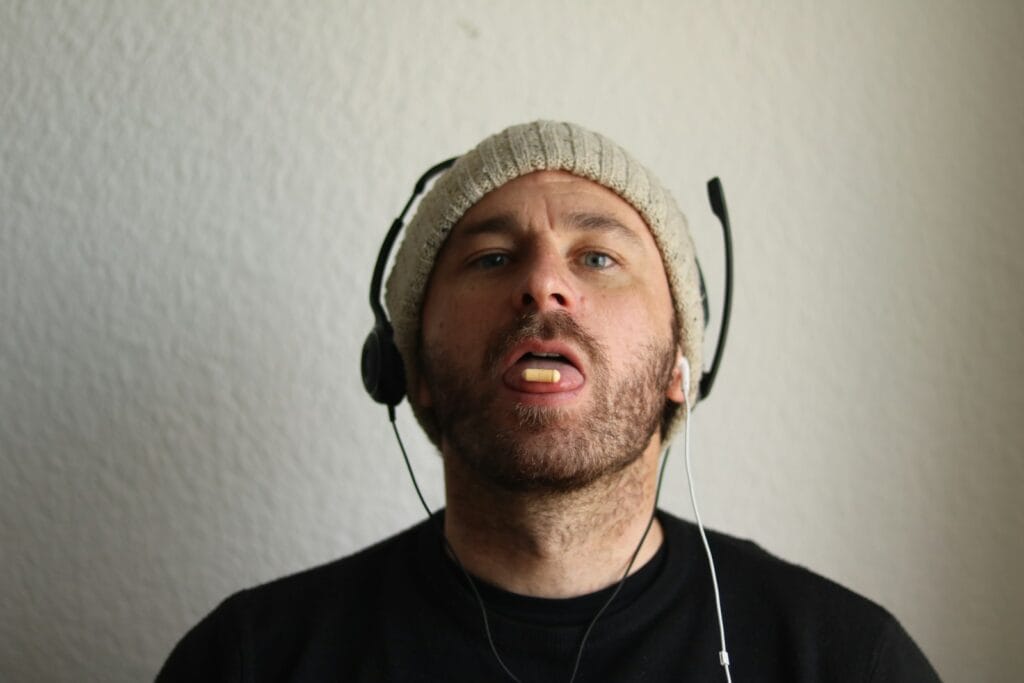 Man wearing headphones and beanie, holding food in mouth.