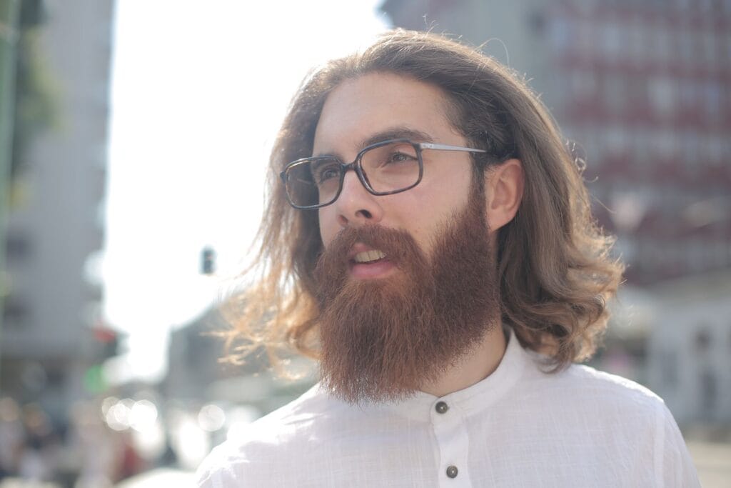 Close-up of a fashionable bearded man wearing glasses outdoors in sunlight.