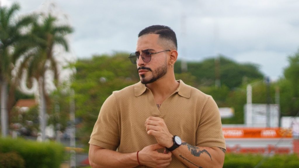 Man in sunglasses and polo shirt adjusts sleeve.